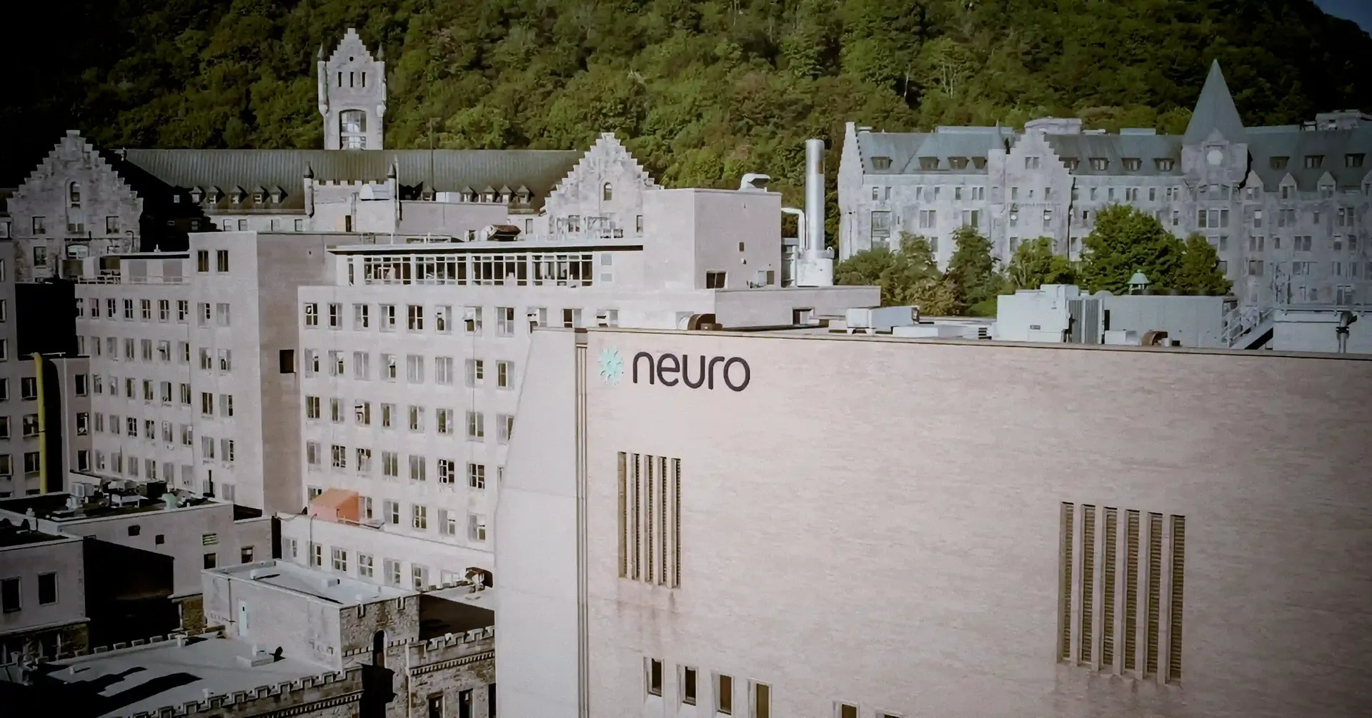 Photo of the Neurological Institute next to Mount Royal mountain in Montreal with the green of the mountain in the background with the Institute and hospital in the foreground